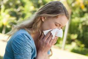 Woman blowing nose with tissue paper at park